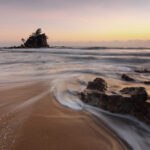 Strand, Sonnenuntergang, kleine Steinklippe mit Baum darauf in der Ferne